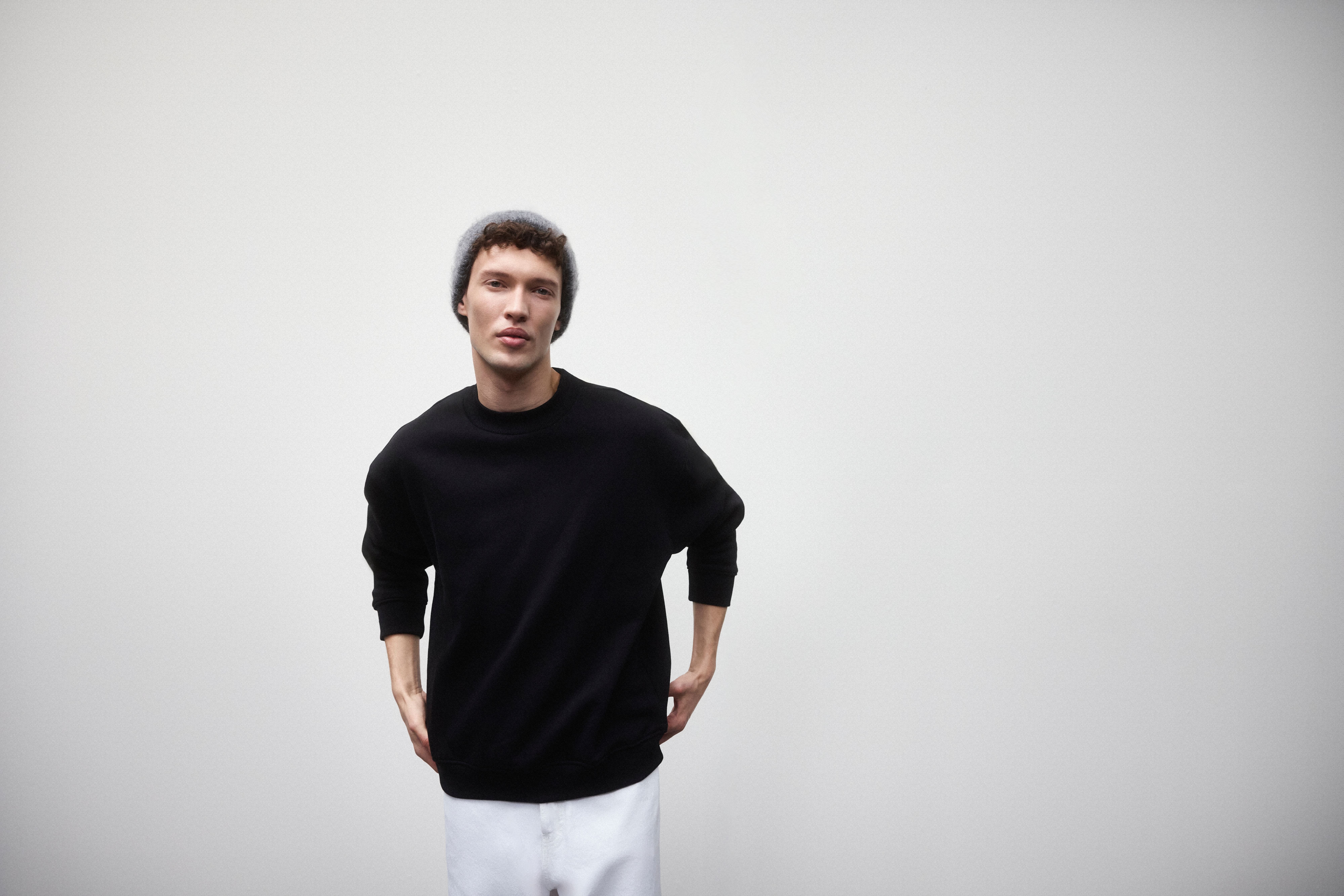 Muž oblečený v čiernej mikine, bielych džínsoch a sivej čiapke